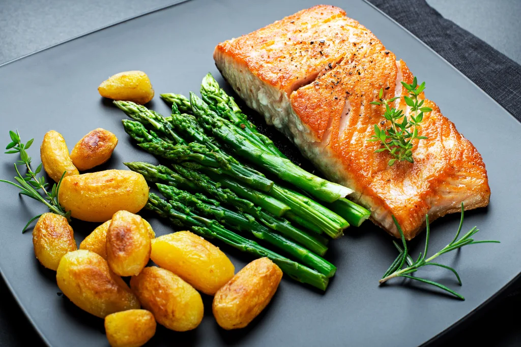 Roasted salmon fillet with asparagus and potatoes on black background