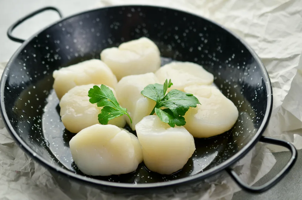 Raw scallops with herbs on frying pan